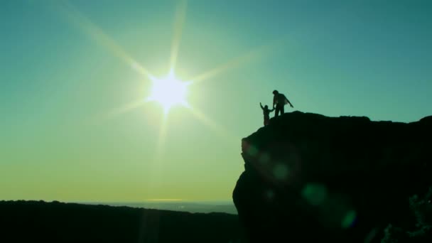 Rock. Silhouette. The man with her child standing on the edge of the cliff. Then enthusiastically raises his hands. — Stock Video