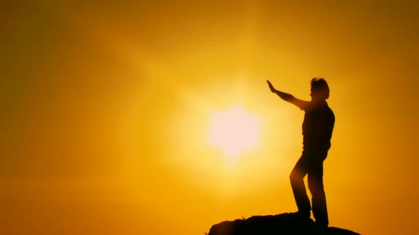 Felle zon. silhouet. beweging zoom. een man staat op de rand van een klif en kijkt naar de zon door zijn hand. — Stockvideo