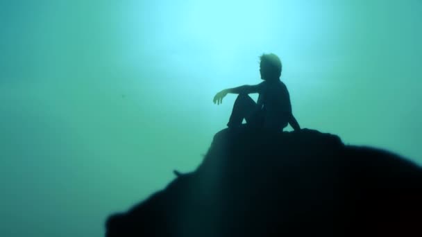 Blaue Sonne. Bewegungszoom. Silhouette. ein Mann sitzt am Rande der Klippe. — Stockvideo