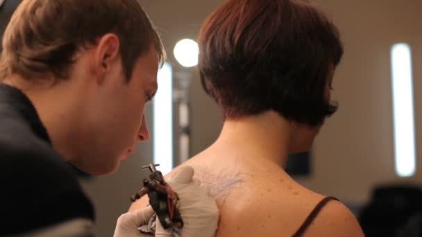 Мужчина рисует татуировку на спине девушки . — стоковое видео