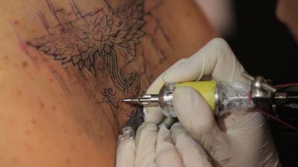 Muž maluje tetování na zádech dívky. — Stock video