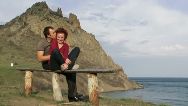 Couple flirting. Young couple in love sitting on the bench on the hill near the sea. Couple flirting in nature. — Stock Video