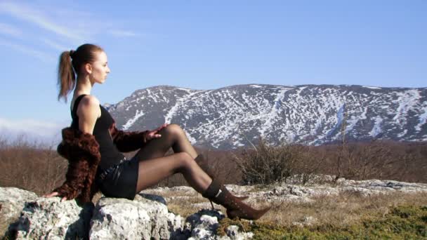 Mujer en las montañas. Hermosa modelo de moda chica sentada en una roca contra el hermoso paisaje natural. Dos cuadros. Primer plano . — Vídeo de stock