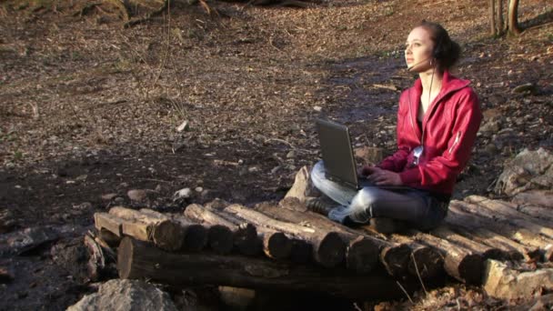 Frau arbeitet mit Laptop an der Natur. Frau druckt auf dem Laptop im Hintergrund eines schönen Waldes. — Stockvideo