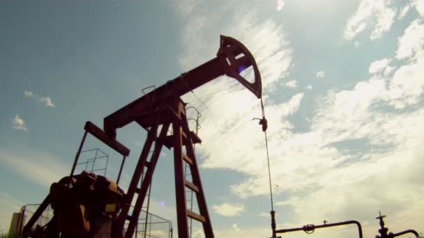 Oljeproduktionen. oljerigg extraherar resurser från jorden. i bakgrunden en vacker blå himmel. — Stockvideo