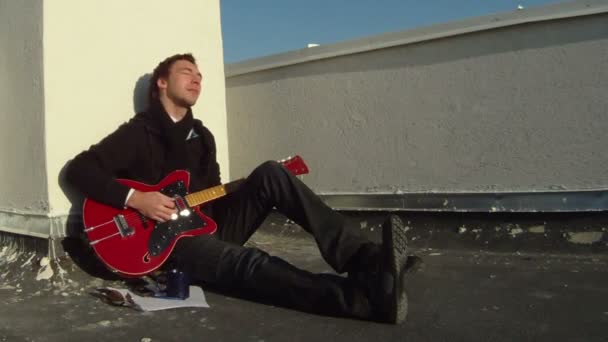 En man sitter på golvet och spelar gitarr — Stockvideo