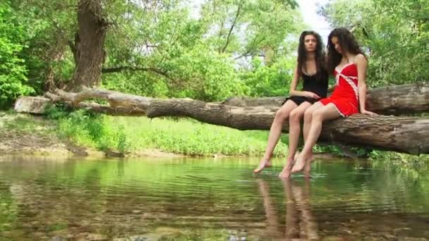 Sisters sitting on a riverside and splashing — Stock Video