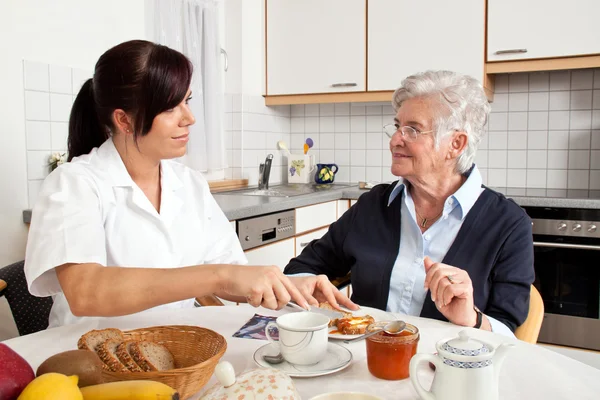 Nurse helps elderly woman at breakfast Royalty Free Stock Images