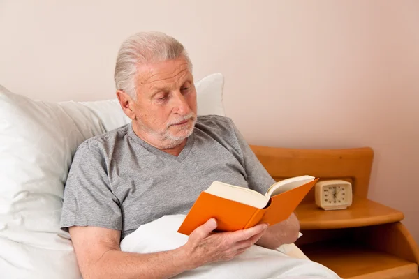 Senior på ett vårdhem när bokar i sängen — Stockfoto