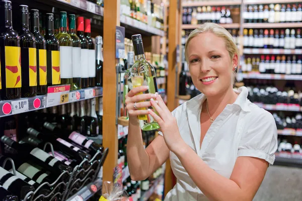 Mulher com prateleira de vinho de um supermercado — Fotografia de Stock