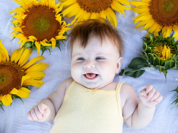 美丽可爱的五个月的微笑的白人女孩躺在向日葵上 免版税图库照片
