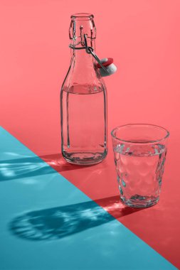 Güneş ışığı gölgeli vintage şişe ve cam ya da pembe-mavi arka plan yansıması, soyut.