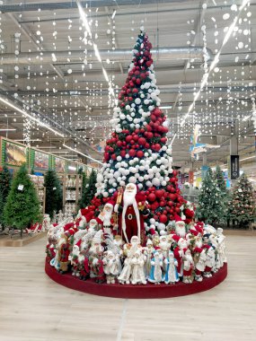 Dnipro, Ukrayna - 14 Kasım 2021: Kırmızı ve beyaz toplarla süslenmiş yüksek Noel ağacı. Noel ağacının etrafında Noel Baba ve Kar Bakireleri bebekleri var. Alışveriş merkezine yerleştirilmiş. Noel ve Yeni Yıl 'dan Önce Dekorasyonlar