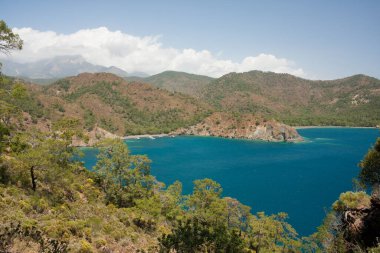 Resimli bir manzara. Tepeden Akdeniz manzarası var. Dağlar ve tepelerle çevrili deniz koyunun kartpostal görüntüsü. Yürürken Lycian Yolu, Antalya, Kemer, Türkiye. Bahar