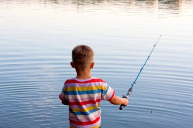 young fisherman is fishing in river on summer day. boy threw bait and is waiting for bite, standing with his back to camera. Amateur fishing in open water. Nature. Happy and interesting childhood