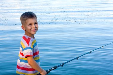Portrait of smiling preschool boy. Happy child is fishing in river on summer day. boy threw fishing rod and is waiting for bite. Amateur fishing in open water. Nature. Happy childhood. copy space