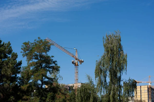 Tower cranes are building house. High crane against blue sky on sunny summer day. flag of Ukraine is on crane cab. Concrete building under construction. Construction site