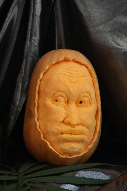 Cadılar Bayramı balkabağı siyah arka planda yakın plan. Bir adamın yüzü bir balkabağına oyulmuştur. Cadılar Bayramı 'nın balkabağı sembolü