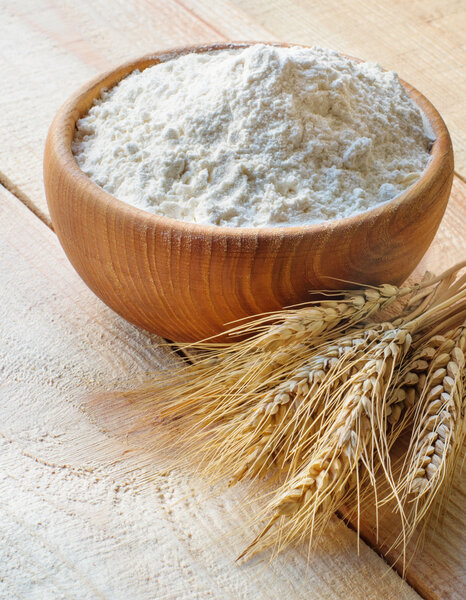 Wooden bowl full flour and wheat ears on wooden background