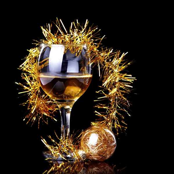 Glass with drink, a Christmas ball and tinsel. — Stock Photo, Image