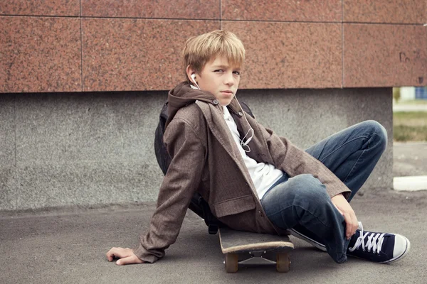 Škola teen sedí na skateboardu v blízkosti školy — Stock fotografie