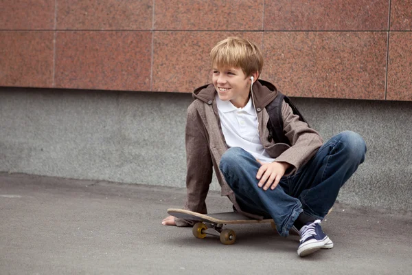 Škola teen sedí na skateboardu v blízkosti školy — Stock fotografie