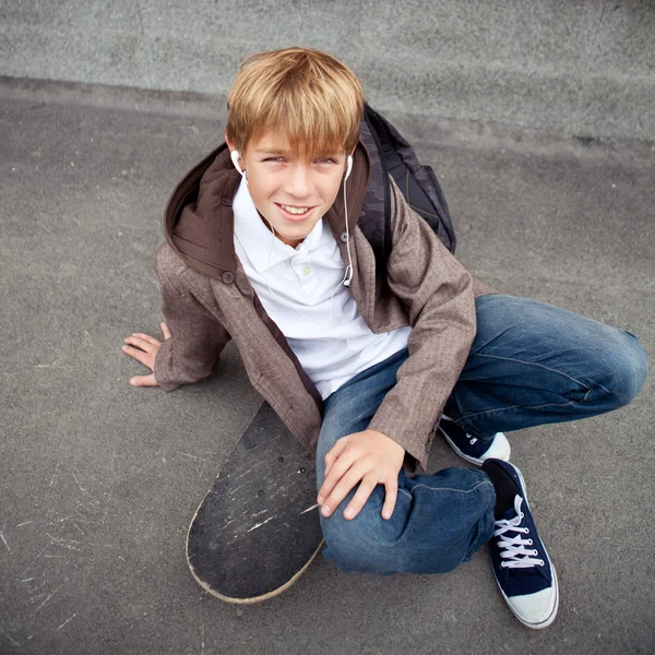 Škola teen sedí na skateboardu v blízkosti školy — Stock fotografie