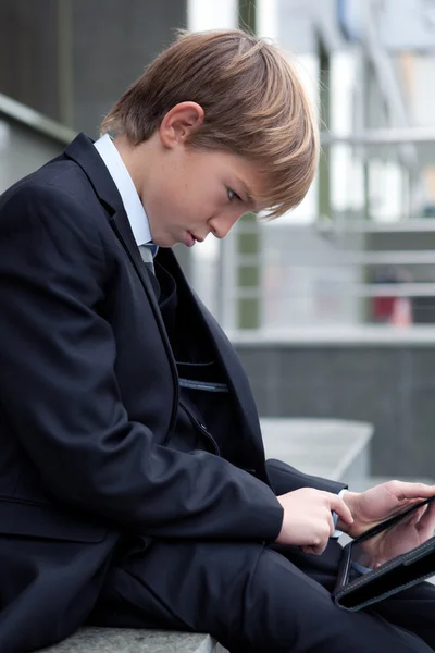 Skola pojke med elektroniska tablett sitter, — Stockfoto