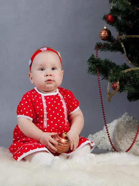 Little girl in red dress sitting near Christmas tree — Stock Photo, Image