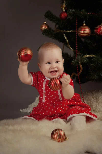 Kleines Mädchen in rotem Kleid sitzt neben Weihnachtsbaum — Stockfoto