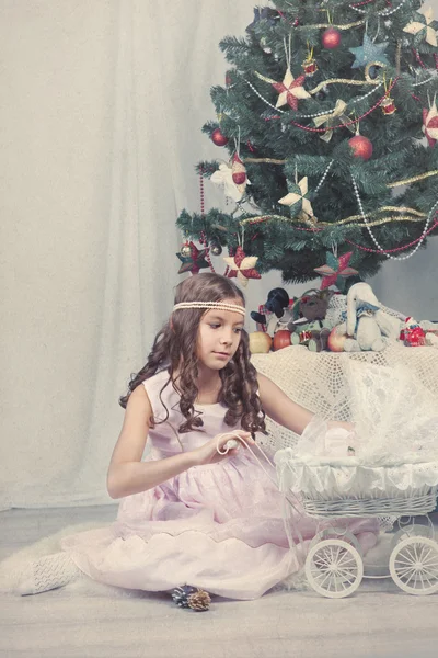 Dívka hraje s panenkou kolem vánočního stromu — Stock fotografie
