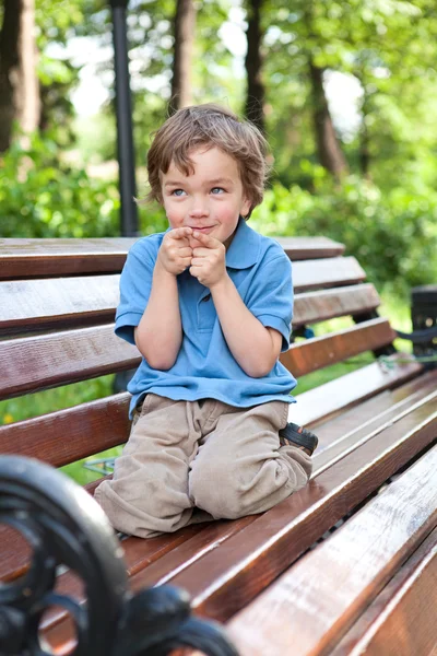 Menino senta-se no banco no parque — Fotografia de Stock