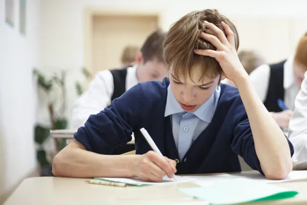 Menino da escola lutando para terminar o teste em sala de aula . — Fotografia de Stock