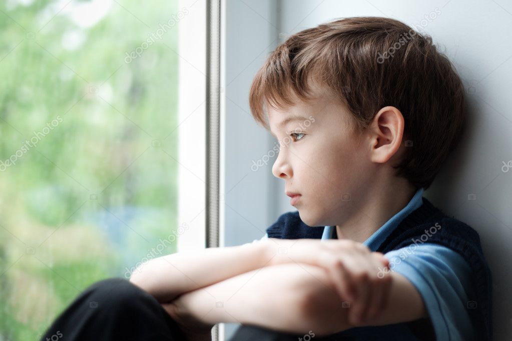 Sad boy sitting on window