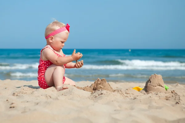 Little girl sitting on sand at beach — Stock Photo, Image