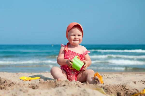 Little girl sitting on sand at beach — Stock Photo, Image