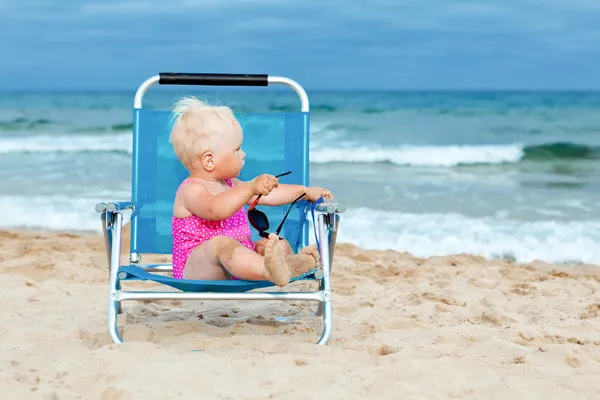 Onnellinen pieni tyttö istuu tuolilla rannalla — kuvapankkivalokuva