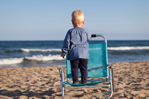 Glückliches kleines Mädchen steht auf Stuhl am Strand — Stockfoto