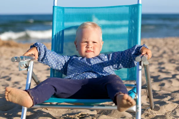 Feliz niña sentada en la silla en la playa — Foto de Stock