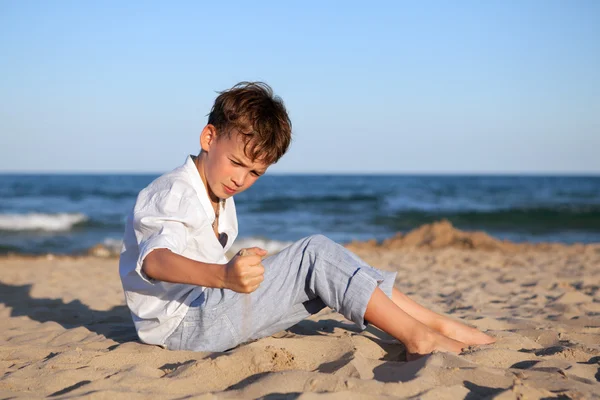 Nadenkende jongen zittend op zand op strand — Stockfoto