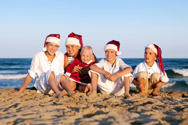 Children in santa claus hat are sitting on beach — Stock Photo, Image