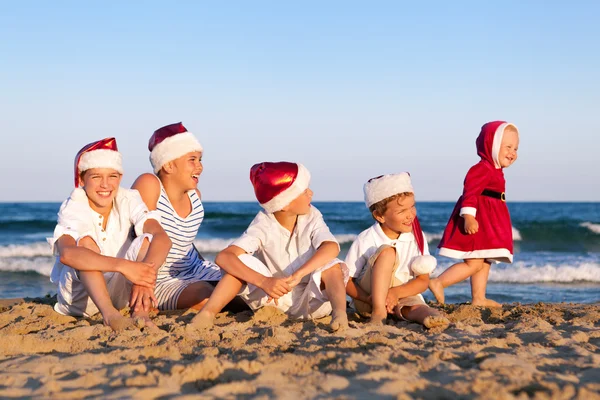 Dzieci w santa claus kapelusz siedzą na plaży — Zdjęcie stockowe