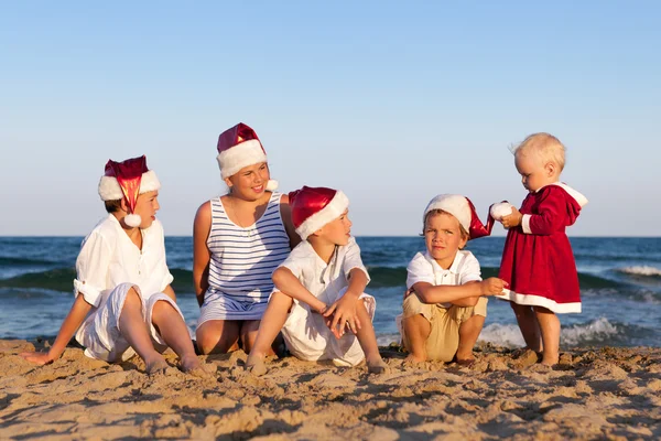 Dzieci w santa claus kapelusz siedzą na plaży — Zdjęcie stockowe