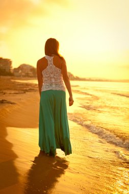 gün batımında kumsal boyunca yürüyen güzel bir kız