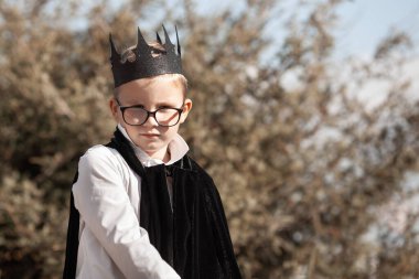 Sonbahar yapraklarının arka planında cadılar bayramı kostümü giymiş gözlüklü bir çocuğun portresi.