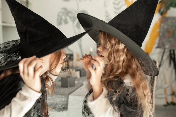 ハロウィンパーティーで魔女の衣装を着た2人の女の子 子供たちは黒い帽子をかぶっている 彼らはささやく — ストック写真