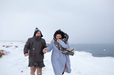 Birbirine aşık bir çift kış denizi kıyısında yürüyor, bir erkek ve bir kadın donmuş, kar yağıyor.