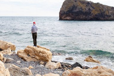 Adam kıyıda balık tutuyor, çocuk elinde dönen bir çubuk tutuyor.