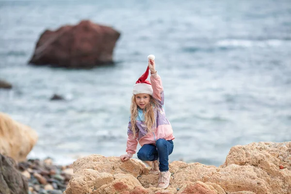 Deniz Kıyısında Noel Baba Şapkalı Küçük Güzel Kız Ceketli Bir — Stok fotoğraf