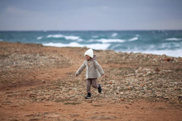 这孩子穿着毛皮外套 头戴白帽 沿着冬季的海滨散步 — 图库照片